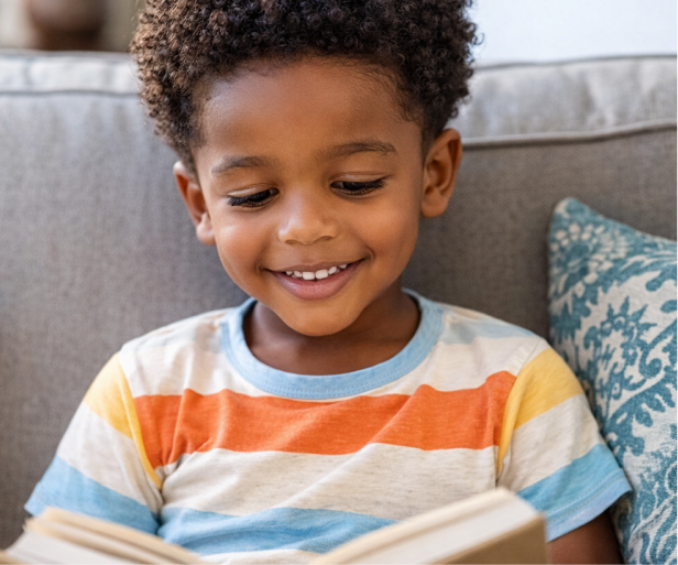 Young boy reading a book on a couch in a colorful striped shirt